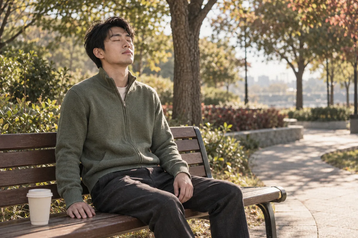 A young man in a green zip sweater taking a slow breath on a park bench in the morning sun. Coping with OCD.